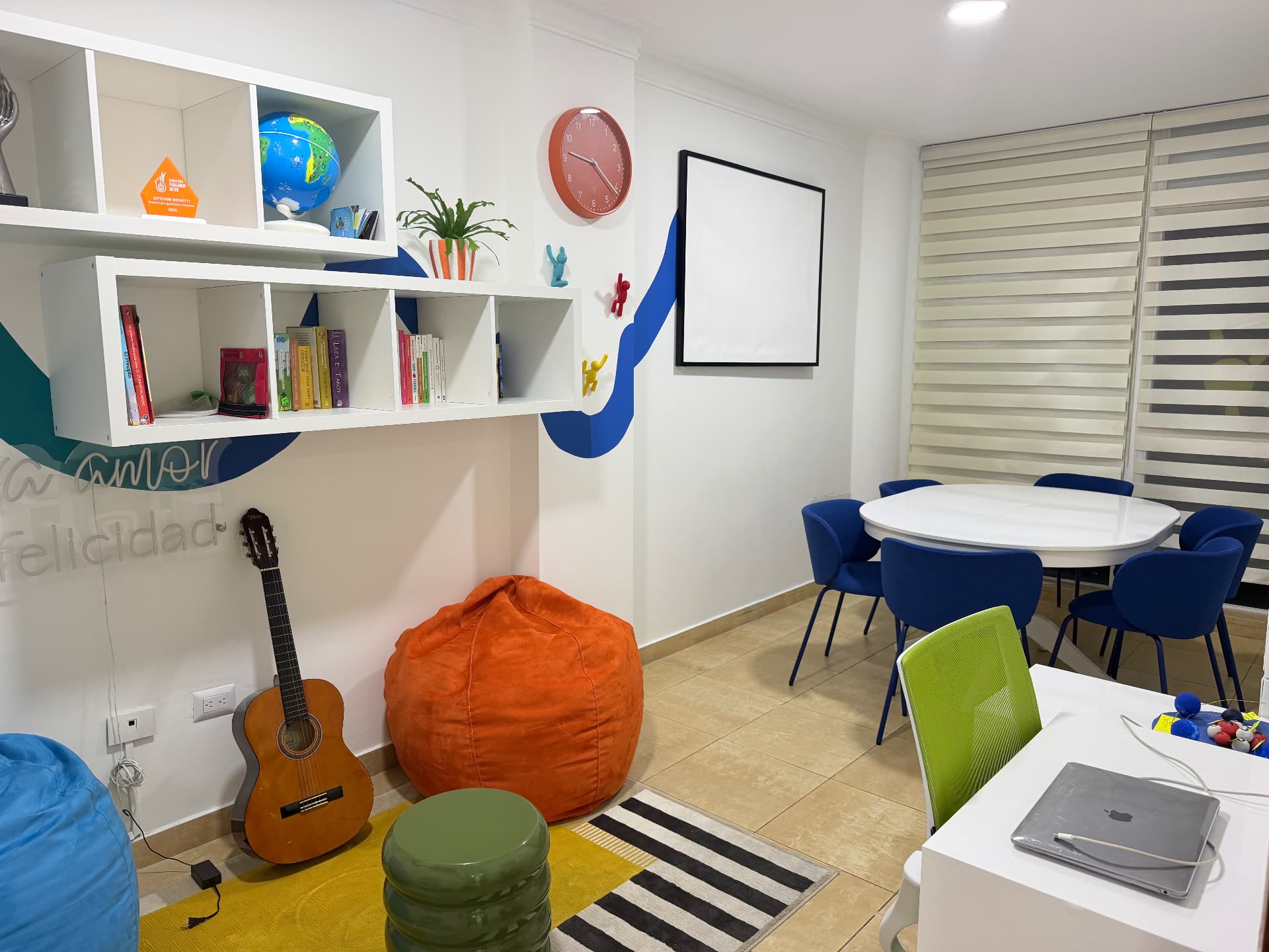 Fotografía real del aula de EDUSER con biblioteca, guitarra, asientos y mesa de trabajo